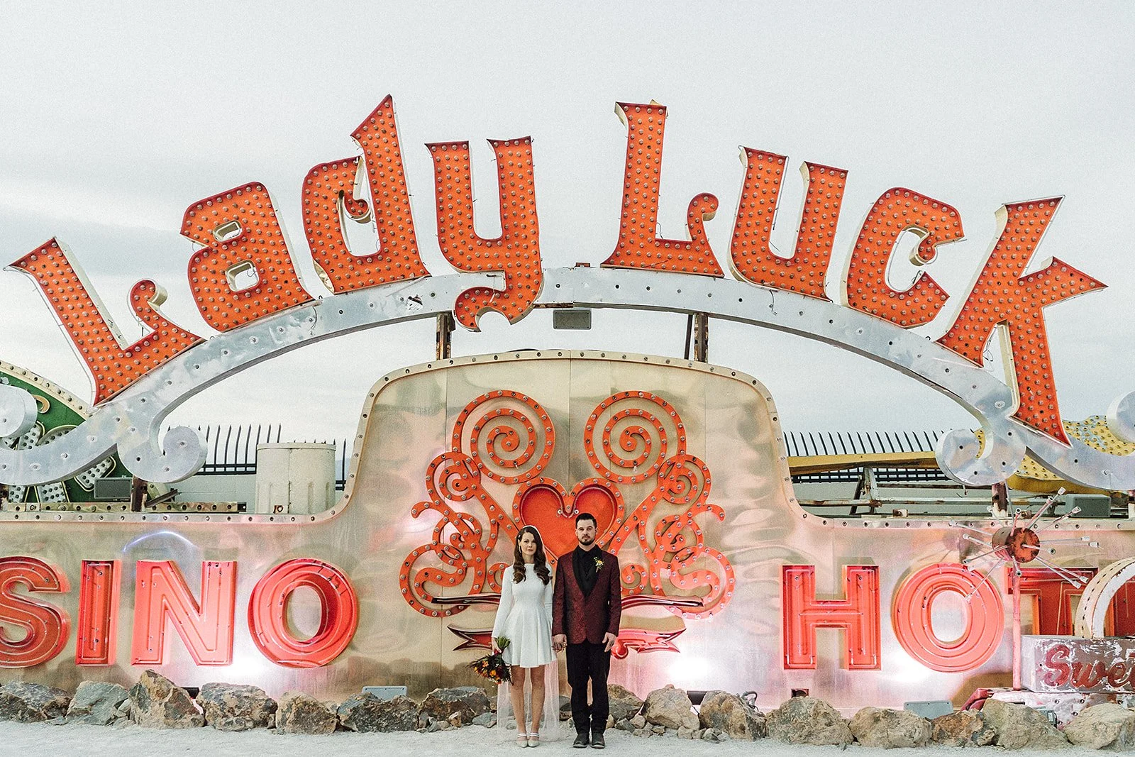 Couple standing hand in hand after eloping in front of the Lady Luck Sign at The Neon Museum.